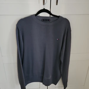 Grå tröja från Tommy Hilfiger L - Snygg grå tröja från Tommy Hilfiger i storlek L. Klassisk rund halsringning och diskret logga på bröstet. Perfekt basic-plagg med lång ärm och mjukt material som känns skönt mot huden. Passar M också