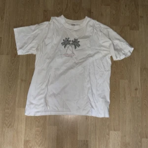 Vit t-shirt med palmtryck från 157 - Vit t-shirt från 157 i storlek L, tillverkad i 100% bomull. Framtill finns ett stilrent tryck med två palmer och texten 'THE CITY OF PALMS, FORT MYERS, FLORIDA'. Klassisk passform och rund hals. Perfekt för dig som gillar chill och enkel stil.