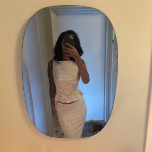 Vit prickig klänning med volang - Supersöt vit kjol och topp med svarta prickar och smockad midja som ger en snygg siluett. Toppen  är ärmlös och har en volangdetalj vid midjan. Perfekt för sommarens alla tillfällen. Sitter tajt men ändå bekvämt och har tyvärr inte komma till användning 