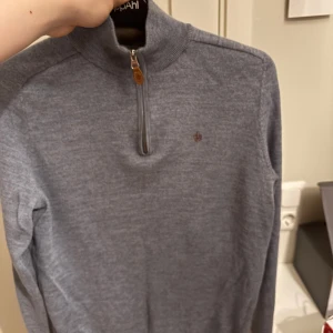 Blå polotröja Morris i merinoull - Står L men passad som M. Snygg gråblå polotröja från Morris i 100% merinoull. Tröjan har half zip med en liten läderdetalj på dragkedjan och diskret Morris-logga på bröstet. Långärmad och med ribbade muddar vid hals, ärmslut och nederkant. Perfekt för dig som gillar stilrena och bekväma plagg.