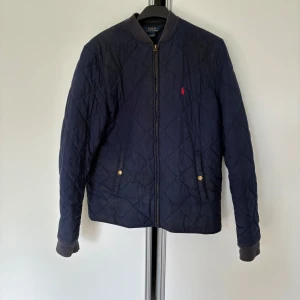 Mörkblå quiltad jacka från Polo Ralph Lauren - Säljer en mörkblå quiltad jacka från Polo Ralph Lauren med guldfärgade knappar vid fickorna och dragkedja framtill. Jackan har ribbade muddar och en liten röd logga på bröstet. Storlek xl ungdom vilket motsvarar xs/s i herr. Sitter som en S