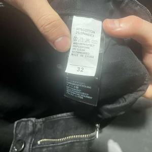 Svarta jeans med tryck från AMIRI - Säljer ett par svarta jeans från AMIRI med coolt ängel-tryck och slitningar på framsidan. Jeansen har dragkedja och är tillverkade i bomull med lite stretch för extra komfort. Perfekta för dig som vill sticka ut med din stil.