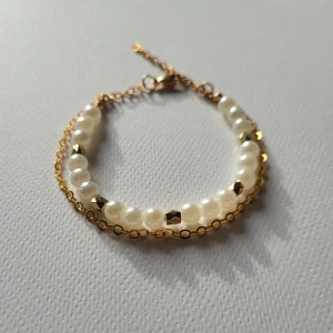 Pärlarmband med guldfärgad kedja - Stilrent armband med vita pärlor och små guldfärgade detaljer, kombinerat med en tunn guldfärgad kedja. Perfekt för att ge en elegant touch till din look.