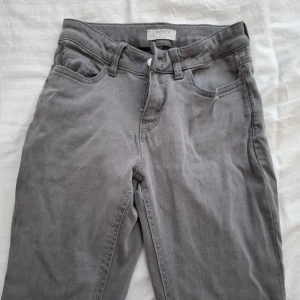 Grå jeansbyxor från Lindex - Säljer ett par grå jeansbyxor från Lindex. Byxorna har normal passform och stängs med dragkedja och knapp. Perfekta till vardags för en stilren look.