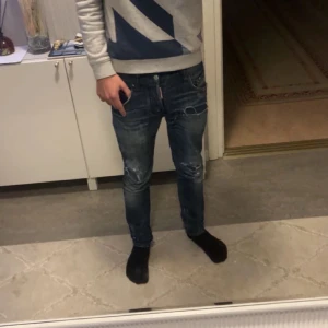 Blå Dsquared2 jeans med slitningar - Säljer ett par blå jeans från Dsquared2 med snygga slitningar och detaljer på benen. Jeansen har slim passform och klassisk femficksdesign. Märkeslapp bak i midjan. Perfekta för dig som gillar streetstyle. Små tecken på användning men allmänt väldigt bra skick. 