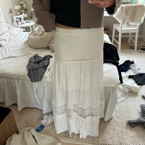 Vit långkjol med spetsdetaljer - Säljer en vit långkjol med spets, perfekt nu till sommaren. En inbyggd extra kjol under så inte genomskinlig. Resår i midjan. Lite skrynklig på bild då jag inte strykt den efter tvätt