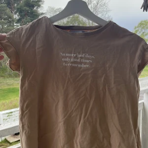 Beige t-shirt med tryck från 157 - Beige t-shirt från 157 med vitt tryck på bröstet där det står 'No more bad days, only good times to remember'. Klassisk rund hals och korta ärmar. Perfekt för en avslappnad stil.