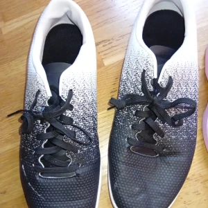 Svarta och vita fotbollsskor med snörning - Säljer ett par fotbollsskor i svart och vitt med snyggt färgskiftande mönster. Skorna har klassisk snörning och rund tå. Perfekta för dig som vill sticka ut på planen.