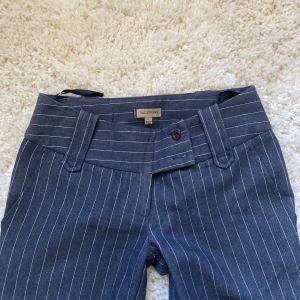 Mörkgrå randiga lågmidjade kostymbyxor - Snygga mörkgrå kostymbyxor med vita tunna ränder. Byxorna har bred linning, bälteshällor och bootcut-modell. Perfekta för en dressad look och passar till många olika stilar. Passar någon som är Max 167 skulle jag säga💘💘