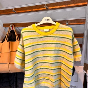 Randig stickad tröja från American Vintage - Supermjuk stickad tröja från American Vintage med gula, gröna och vita ränder. Tröjan har korta ärmar och rund halsringning med gul kant. Perfekt för dig som gillar färg och en avslappnad stil. (Har en liten foundation-fläck på sig) 