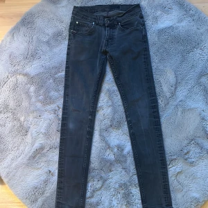 Svarta/gråa Tiger of Sweden jeans - Säljer ett par svarta skinny jeans med lätt tvättad look och klassiska fem fickor. Jeansen har dragkedja och knapp i midjan samt smala ben. Perfekta för dig som gillar en tajt passform och stilren look. W28/L32