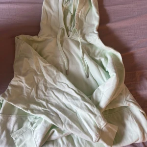 Ljusgrön hoodie från H&M - Säljer en ljusgrön hoodie från H&M i storlek XS. Tröjan har huva med dragsko och en stor magficka framtill. Perfekt för en avslappnad stil och enkel att matcha med jeans eller leggings.
