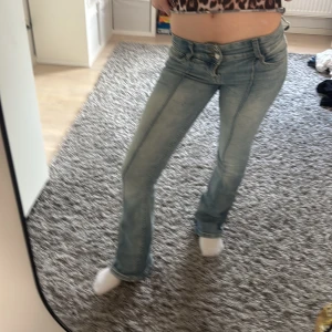 Ljusblå bootcut jeans - Säljer ett par ljusblå jeans med bootcut-modell och låg midja. Jeansen har klassiska fickor fram och bak samt synliga sömmar längs benen. Perfekta för dig som gillar en retroinspirerad stil.