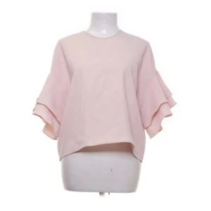 Ljusrosa volangblus från Zara Woman - Supersöt ljusrosa blus från Zara Woman med volangdetaljer på ärmarna. Blusen har en lös passform och korta ärmar med dubbla volanger. Perfekt för en fräsch och feminin look.