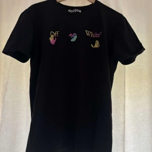 Svart t-shirt från Off-White med färgglada tryck - Svart t-shirt från Off-White med färgglada hand- och texttryck på bröstet samt stora pilar i olika färger på ryggen. Klassisk passform och rund hals. Perfekt för dig som gillar streetwear och vill sticka ut.