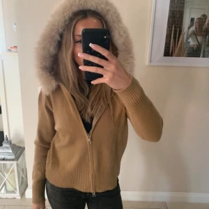 Beige jacka med fuskpälsluva - Säljer en beige jacka med dragkedja och stor luva med fuskpäls. Jackan har ribbade muddar och är långärmad. Alessa s liknande kofta / jacka. Nyskick (använd en gång). Storlek M men passar som S.