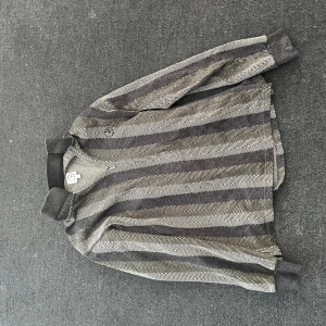 Grå, svart och mörk grön randig half zip ifrån Polar - Säljer en grå och svart randig half zip ifrån Pplar med ribbade muddar och krage. Tröjan har långa ärmar och ett diskret mönster som ger en stilren look. Perfekt för dig som gillar en avslappnad men snygg stil. Använd ett par fåtal gånger