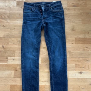 Mörkblå slim fit jeans Glenn - Snygga mörkblå jeans i slim fit-modell, Glenn. Klassisk femficksdesign med knappar i gylfen och kontrastsömmar. Jeansen har en smal passform och är tillverkade i ett mjukt denimtyg som sitter skönt hela dagen.