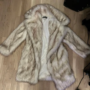 Ljus pälsjacka med huva - Säljer en fluffig och lyxig ljus pälsjacka med huva från Chicy. Jackan har långa ärmar och är fodrad på insidan. Perfekt för att hålla värmen under kyliga dagar och ger en riktigt snygg look.