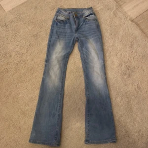 Blå bootcut jeans - Snygga blå bootcut jeans med klassisk femficksdesign och ljusa slitningar framtill och baktill. Jeansen har normal passform och stängs med knapp och dragkedja. Perfekta för en avslappnad och trendig look. små i storleken