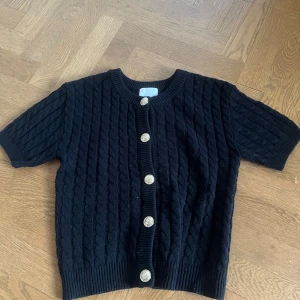 Svart stickad kofta med kort ärm och guldknappar - Säljer en svart stickad kofta med korta ärmar och snygga guldknappar framtill från H&M i storlek S