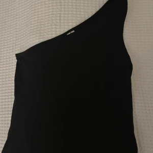 Svart oneshoulder topp från NLY Trend - Säljer en svart oneshoulder topp från NLY Trend i storlek S. Snygg och stilren modell med asymmetrisk axel, perfekt för att skapa en trendig look.