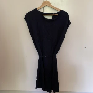 Marinblå klänningmed knytband  - Marinblå enkel klänning från In Extenso med knytband i midjan. Modellen är ärmlös och har en rak, avslappnad passform. Perfekt för dig som gillar minimalistisk stil och vill ha något bekvämt och stilrent nu till sommaren.