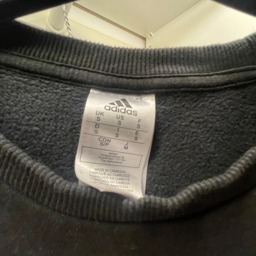 Säljer en svart kortärmad tröja från Adidas knappt använd  med klassiska vita ränder på axlarna och broderad logga på bröstet. Tröjan har rund halsringning och är gjord i mjukt material, perfekt för en sportig look.. Neuletakit & Villapaidat.