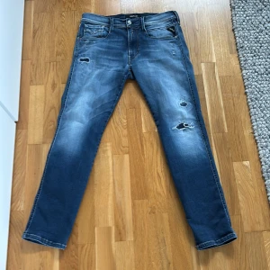 Blå Replay Hyperflex jeans med slitningar - Säljer ett par blå Replay Hyperflex jeans med snygga slitningar och lätt tvättad look. Klassisk femficksmodell. Perfekta för dig som gillar en avslappnad men trendig stil.