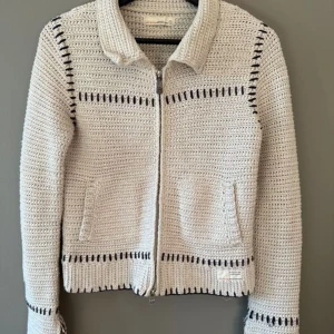 Beige stickad stickad tröja med dragkedja från Odd Molly - Säljer en beige stickad tröja från Odd Molly med svarta dekorativa sömmar. Jackan har dragkedja framtill, krage och två fickor. Perfekt för lager-på-lager och har en snygg, avslappnad look.det står inte stolek, (stolek 2 står på lappen)