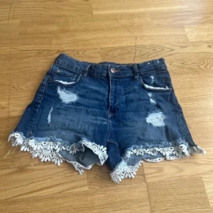 H&M Blå jeansshorts med spetsdetalj Size M-S - Snygga blå jeansshorts med slitna detaljer och vit spets längs bensluten. .