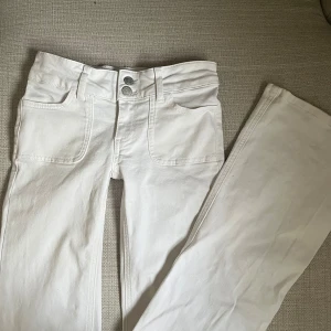 Lågmidjade bootcut jeans - Säljer mina vita lågmidjade bootcut jeans med dubbla knappar fram. Perfekta för en stilren look. Säljer då de inte kommer till användning! Använda fåtal gånger och känns helt nya! Storlek 32, innerbenslängd 77cm och gren 16/17 cm. De har en liten brun fläck längst ner vid hälen (se bild 3) men inget som syns! 