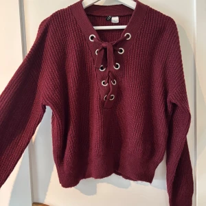 Vinröd stickad tröja - Säljer en vinröd stickad tröja från Divided med snygg snörning framtill!