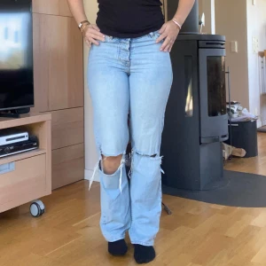 Ljusblå slitna jeans med raka ben midwaist  - Ljusblå jeans med raka ben och stora slitningar vid knäna. Klassisk femficksmodell med normal passform och midwaist. Jeansen har en avslappnad vibe och är perfekta för en trendig look. Är nog ännu snyggare om det är lite stora så det blir lite mer hängande på höfterna och därav lägra i midjan. Jag på bilderna har vanligtvis S