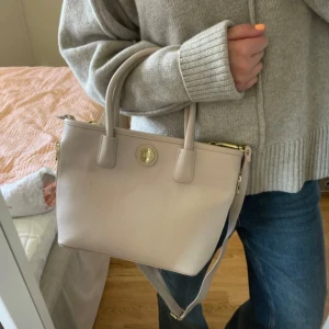 Handväska - Beige gullig handväska med justerbart axelremsband. Använd fåtal gånger och i mycket bra skick. Flera fack innuti och utanpå, perfekt till skola och jobb