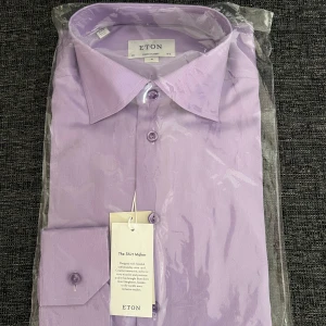 Ljuslila skjorta från Eton - Säljer en stilren ljuslila skjorta från Eton med klassisk krage och knäppning framtill. Skjortan är långärmad och tillverkad i ett tunt, elegant tyg som passar perfekt till en dressad look.