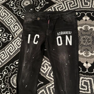  DSQUARED2 ICON jeans  -  Svarta DSQUARED2 ICON jeans i storlek [54/38]. Jeansen har en cool design med vita bokstäver och distressed detaljer samt vita färgstänk. De är i mycket gott skick och perfekta för en trendig och stilren look. 