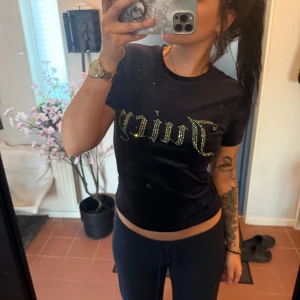 Juicy Couture T-shirt - Säljer en svart tight t-shirt från Juicy Couture med glittrig guldfärgad text på bröstet. T-shirten har rund halsringning och korta ärmar. 