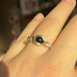 Handgjord silverring med blå guldsten - Unik ring i silverfärgad metall med en glittrig mörkblå sten. Ringen har en tvinnad design runt stenen som ger ett bohemiskt och elegant intryck. Perfekt accessoar för att lyfta din stil.