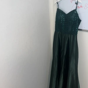 Mörkgrön klänning  - Säljer en elegant mörkgrön långklänning med smala axelband. Överdelen är dekorerad med glittriga paljetter i rutmönster och kjolen är i ett glansigt, slätt material. Perfekt för bal eller festliga tillfällen. Själv hade jag denna i balen i 9:an så den har bara använts en gång sen dess! 🫶orginalpris är 2000kr, men säljer för 700. Hör av dig om du är intresserad. Är förresten 166 cm och passade bra. Men om du är längre än mig  kommer den passa ännu bättre 🫶