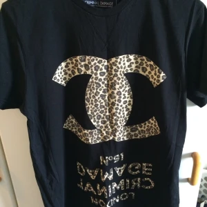 Svart t-shirt med leopardmönster från Criminal Damage - Säljer en svart t-shirt från Criminal Damage med stort leopardmönstrat tryck framtill. T-shirten har rund halsringning och korta ärmar. Perfekt statement-plagg för dig som gillar djurmönster och streetwear.