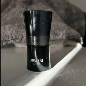 Armani Code Parfym - Elegant och stilren parfymflaska från Armani Code i svart med en glansig finish. Flaskan har en smal midja och bredare topp, vilket ger den ett modernt och sofistikerat utseende. Perfekt för den som söker en tidlös doft.