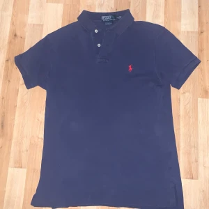 Marinblå Ralph lauren piké  - Hej! Säljer denna marinblåa Ralph lauren piké för att den inte kommer till användning. Den har legat i garderoben i några år utan att blivit rört tills förra sommaren. Har använt den i några månader nu tills sömnen blev riven av min kompis som man kan se på bilden. Den är i storlek S och skicket är bra/ok. Lösningen till sömnen är att antingen vika ihop den så ingen ser det. Eller sy ihop den. Kan gå ner i pris vid snabb affär och skriv om ni har några funderingar🤝. 