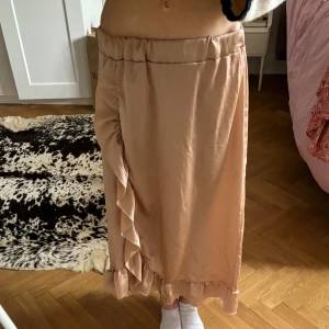 Långkjol med volang - Roséguld-färgad långkjol med volang i satin! Vet tyvärr inte vilket märke men köpte i en liten boutique-butik i Göteborg, står inte heller storlek men skulle säga S/M! Har även resår i midjan💛200 kr + frakt