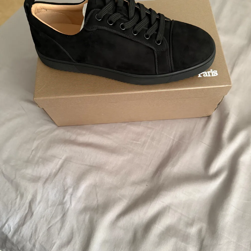 Säljer ett par svarta sneakers från Christian Louboutin med klassisk röd sula och snörning. Skorna är i mocka och har en stilren design med rund tå. Perfekta för dig som vill ha något exklusivt och snyggt till vardags.. Kengät.