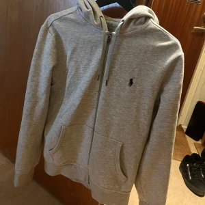 Grå zip up hoodie från Polo Ralph Lauren - Säljer en skön grå zip up hoodie från Polo Ralph Lauren. Köpt på Ralph Lauren butiken i nk för ett tag sen men har knappt använt den då den var för liten för mig. Kvitto finns. Nypris 2300 kr. Pris kan diskuteras vid snabb affär🥳