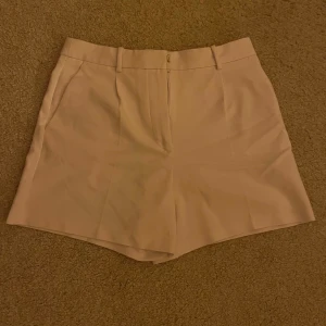 Vita kostymshorts med fickor - Snygga vita shorts med klassisk kostymkänsla. De har normal passform, bälteshällor och diskreta fickor både fram och bak. Perfekta för en stilren look och passar till många olika outfits.