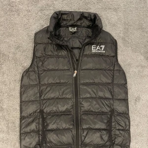 Svart dunväst från Emporio Armani - Snygg svart dunväst från Emporio Armani med dragkedja framtill. Perfekt för lager-på-lager. EA7-logga på bröstet. Det är bara att skriva vid några funderingar svarar snabbt priset är inte heller hugget i sten👍😁🤩