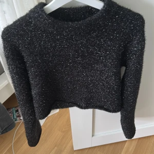 Glittrig svart croppad tröja från H&M - Säljer en svart glittrig croppad tröja från H&M. Tröjan har lång ärm och är perfekt för dig som vill sticka ut lite extra. Materialet är mjukt och stretchigt med en skimrande finish. Snygg att styla till både jeans och kjol. Ordinarie pris 299kr. Använd ett fåtal gånger på nyår. Passar inte jätte bra på mig så den ska inte vara så kort. Storlek xs