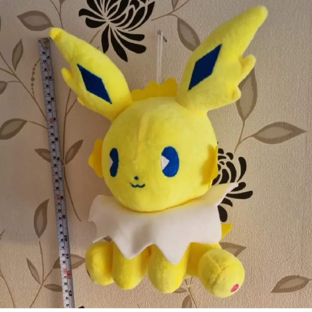 Söt gul och vit mjukisdjur jolteon med stora öron och blå detaljer. Perfekt för samlare eller som en mysig kompis. Den har en vit krage och rosa detaljer på tassarna.. Asusteet.